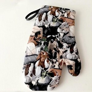 K&ouml;nnte beinhalten: Ein gesteppter Ofenhandschuh mit einem sich wiederholenden Muster aus verschiedenen Ziegen in Braun-, Schwarz-, Wei&szlig;- und Graut&ouml;nen. Der Handschuh verf&uuml;gt &uuml;ber eine schwarze Stoffschlaufe mit kleinen wei&szlig;en Punkten zur praktischen Aufbewahrung.
