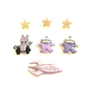 May include: A collection of space-themed embellishments, including a silver robot, two purple aliens, a silver spaceship, and three gold glitter stars. These small decorative items are perfect for crafting or scrapbooking projects.