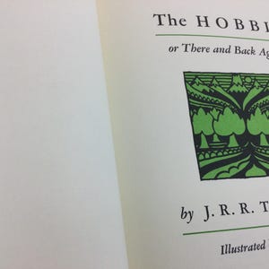 May include: Open book with the title "The Hobbit or There and Back Again" by J.R.R. Tolkien. The cover features a green and black illustration of trees and mountains.