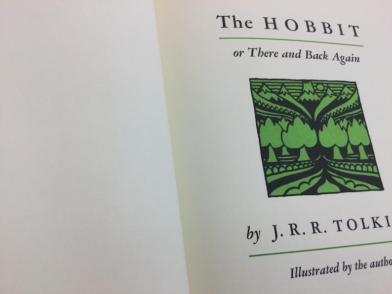 May include: Open book with the title "The Hobbit or There and Back Again" by J.R.R. Tolkien. The cover features a green and black illustration of trees and mountains.