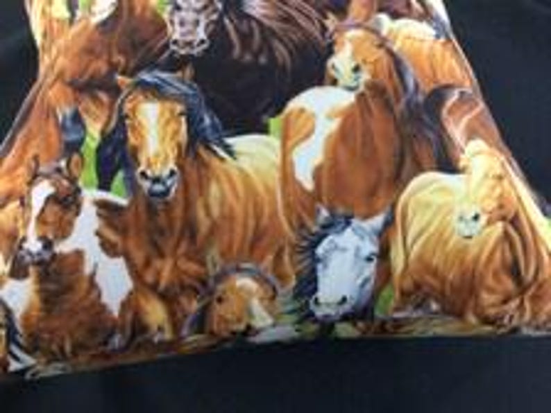 May include: A fabric pillowcase featuring a detailed, colorful print of multiple horses in various shades of brown, chestnut, and white. The horses are depicted in a group, showing different facial expressions and manes against a green background.