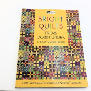 May include: A book titled "Bright Quilts From Down Under" with a yellow cover. The cover features a colorful patchwork design and the text "13 Color-Charged Projects". The book is from "Australian Patchwork and Quilting" Magazine.