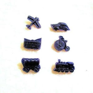 May include: Six small, dark blue game pieces depicting modes of transportation. Included are a biplane, car, stagecoach, bicycle, covered wagon, and a train. The pieces are arranged on a white surface.