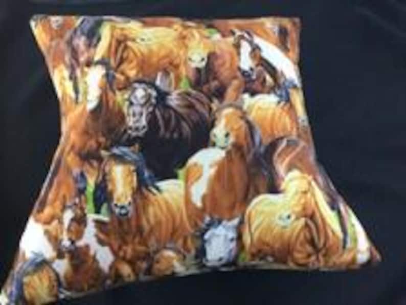 May include: A square throw pillow featuring a detailed, multi-colored print of a herd of horses. The design includes various horse breeds in shades of brown, chestnut, black, and white, depicted in a crowded, overlapping composition.