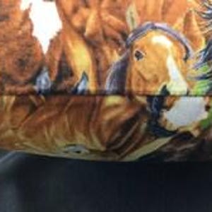 May include: A fabric item featuring a detailed, colorful print of multiple horses. The design includes brown, tan, and white horses with dark manes, set against a background with hints of green, creating a realistic and textured appearance.