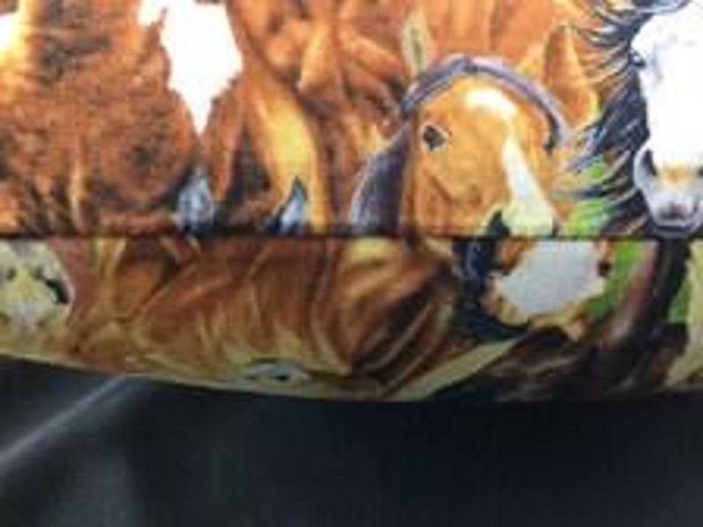 May include: A fabric item featuring a detailed, colorful print of multiple horses. The design includes brown, tan, and white horses with dark manes, set against a background with hints of green, creating a realistic and textured appearance.