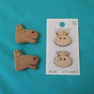May include: Two wooden donkey-shaped buttons with red accents and two monkey-shaped buttons on a white card. The card has the LaMode logo and the text "HOOK 1853". The background is a solid teal color.
