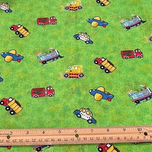 May include: Green fabric with a repeating pattern of various vehicles, including a police car, fire truck, dump truck, airplane, bulldozer, and train. The fabric is measured with a ruler in inches.