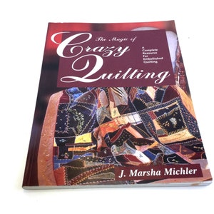 May include: A book titled "The Magic of Crazy Quilting" by J. Marsha Michler. The cover features a burgundy background with the title in a stylized font. The book's cover displays a colorful patchwork quilt with various fabric textures and patterns.