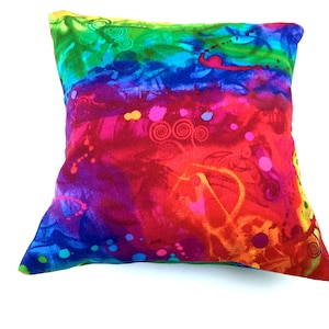 May include: A colorful square pillow with a rainbow tie-dye pattern and abstract designs. The pillow is made of fabric with a soft, textured feel.