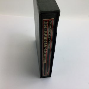 May include: A black book with the title "THE HOBBIT BY J.R.R. TOLKIEN" in white text on a red and gold label. The book is in a black case.