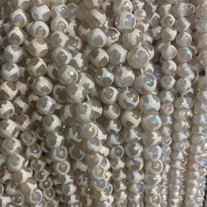 May include: A strand of white agate beads with a translucent, iridescent finish. The beads are round and have a faceted, textured surface.
