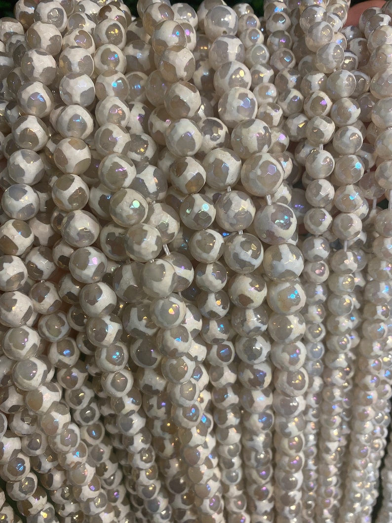 May include: A strand of white agate beads with a translucent, iridescent finish. The beads are round and have a faceted, textured surface.