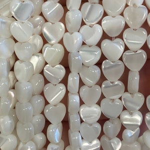 May include: A strand of white heart-shaped beads made from mother of pearl. The beads have a slightly iridescent sheen.
