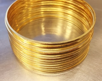 Könnte beinhalten: Ein Stapel goldfarbener Armreifen. Die Armreifen sind rund und haben eine glatte, reflektierende Oberfläche. Der Stapel hat einen Durchmesser von etwa 7,6 cm und ist 5 cm hoch. Die Armreifen sind kreisförmig angeordnet und erzeugen einen geschichteten Effekt.
