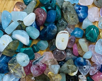 May include: A collection of colorful, natural stone beads with holes drilled through the center. The beads are various shapes and sizes, including round, oval, and irregular shapes. The beads are a mix of colors, including blue, green, pink, purple, and brown.