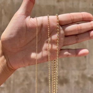 May include: Three gold chains with ball links of different sizes. The chains are laid out on a hand, with the smallest chain on the left and the largest chain on the right.