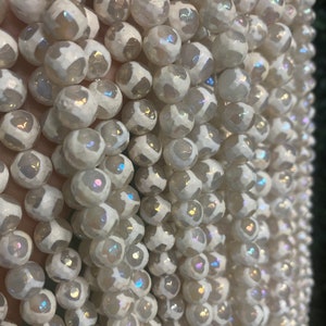 May include: A strand of white agate beads with iridescent shimmer. The beads are round and have a textured surface.