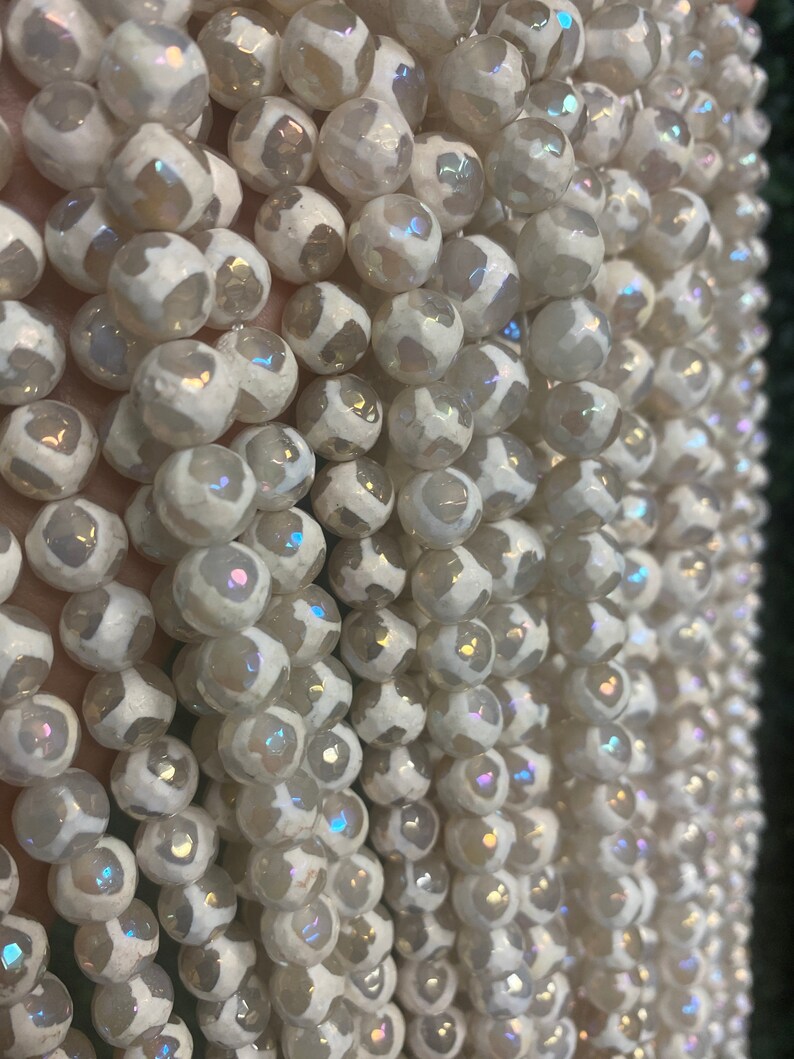 May include: A strand of white agate beads with iridescent shimmer. The beads are round and have a textured surface.