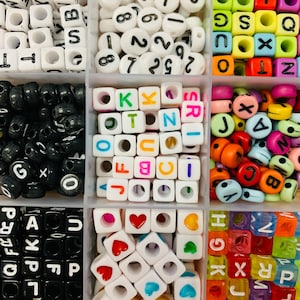 May include: A set of colorful letter beads in a clear plastic storage container. The beads are arranged in rows and columns, with each row containing a different letter of the alphabet. The beads are made of plastic and have a smooth, rounded surface. The container has a clear lid that allows you to see the beads inside.