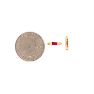 May include: Two small gold-colored jewelry pieces with red and clear stones. One piece is horizontal, the other vertical. A U.S. quarter coin is next to the jewelry for size comparison. The jewelry has a rectangular shape with a red stone in the center and clear stones on each side.