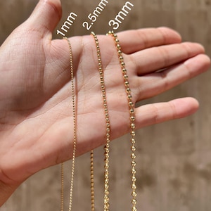 May include: Three gold chains of different sizes, 1mm, 2.5mm, and 3mm, are shown on a hand. The chains are made of small, round beads.