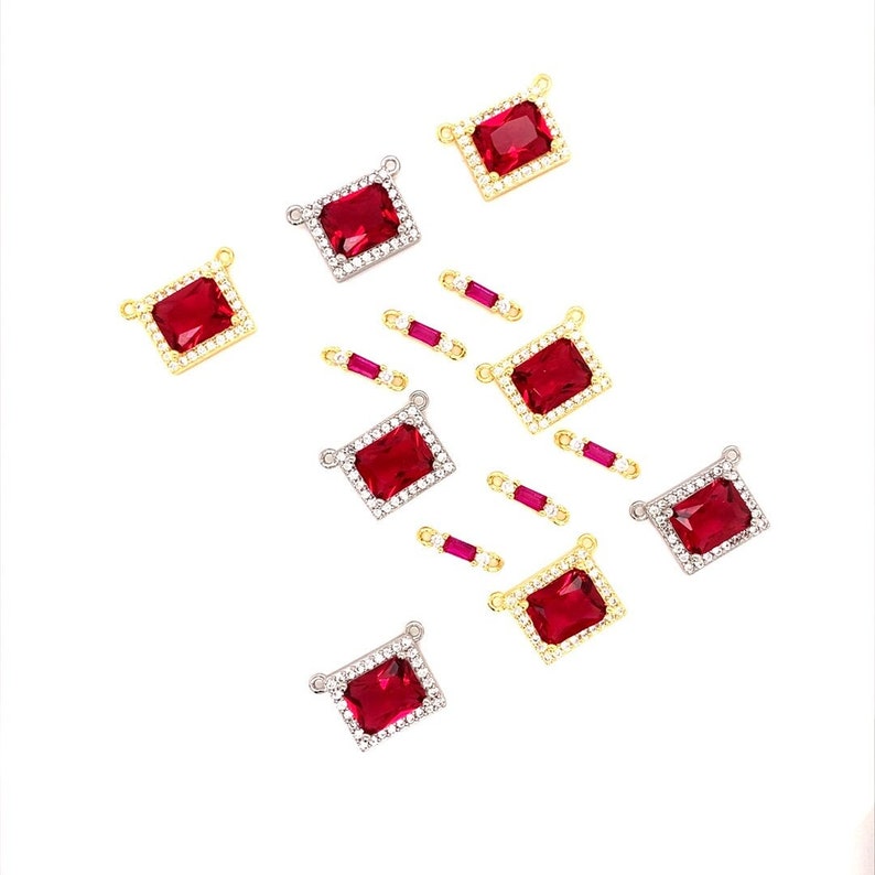 May include: An assortment of rectangular red gemstone charms with gold and silver settings. Some charms are surrounded by small clear stones. Also included are small, rectangular red gemstone charms with gold settings.