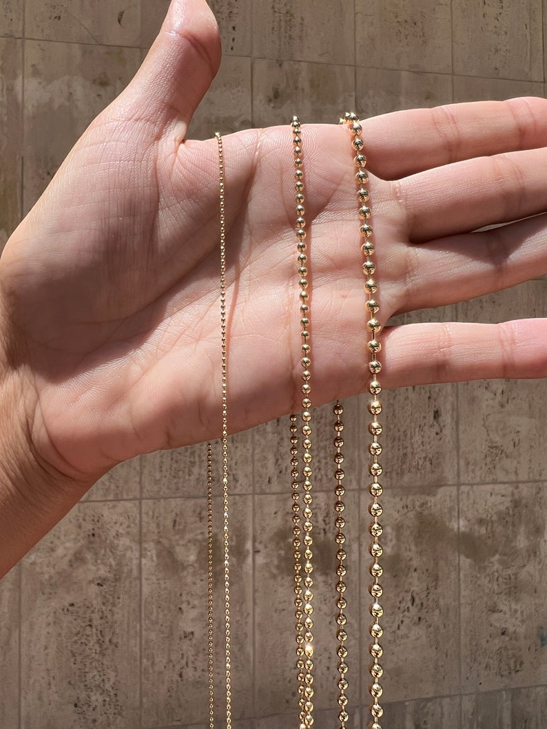 May include: Three gold chains of different lengths and thicknesses. The chains are made of small, round beads.