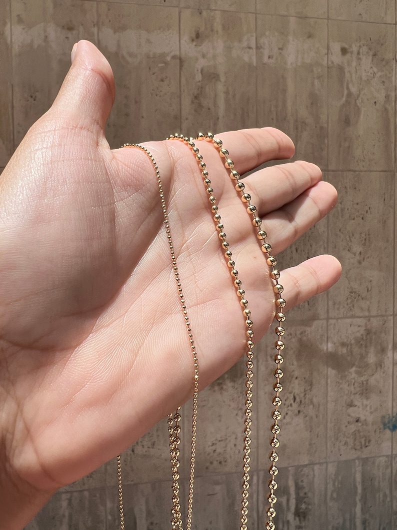 May include: Three gold ball chain necklaces of varying lengths and bead sizes.