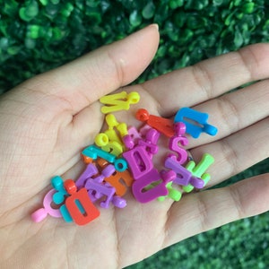May include: A handful of colorful plastic letter beads in various colors, including pink, purple, yellow, orange, blue, and green. The beads are in the shape of uppercase letters.