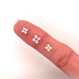 May include: Three flower-shaped nose rings with clear rhinestones. The rings are in silver, rose gold, and gold.