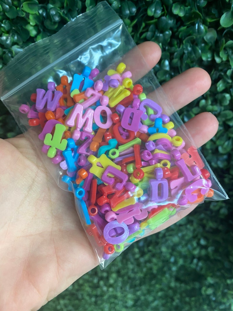 May include: A plastic bag filled with colorful letter beads. The beads are in various colors, including red, yellow, blue, green, and purple. The beads are in the shape of letters of the alphabet.