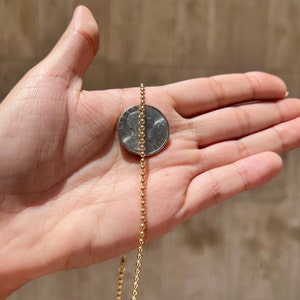 May include: A gold ball chain necklace, shown next to a 25 pence coin for size comparison.