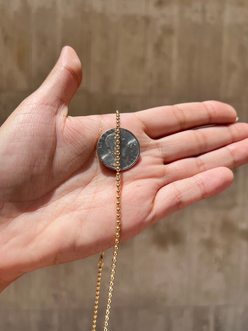 May include: A gold ball chain necklace, shown next to a 25 pence coin for size comparison.