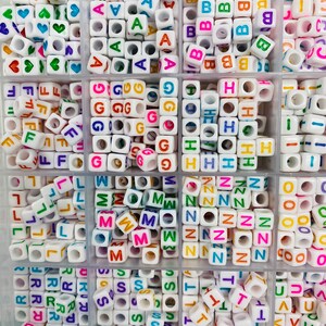 May include: A white plastic storage box filled with colorful letter beads. Each compartment contains a different letter of the alphabet, with the letters A through Z represented.