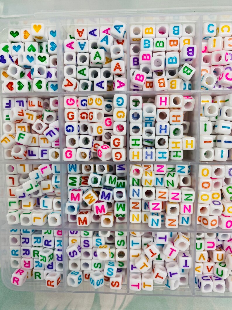 May include: A white plastic storage box filled with colorful letter beads. Each compartment contains a different letter of the alphabet, with the letters A through Z represented.