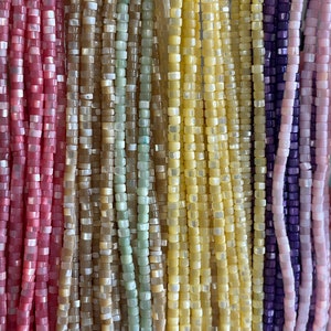 May include: Assortment of colorful square beads made from natural materials. The beads are strung together in long strands and are available in shades of pink, beige, green, yellow, and purple.