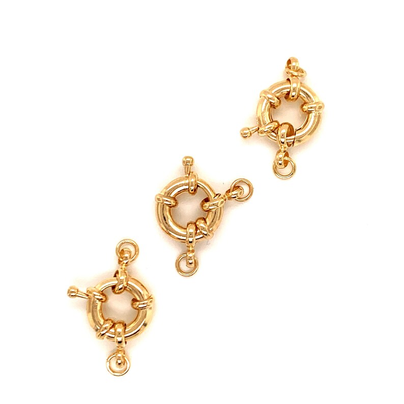 K&ouml;nnte beinhalten: Drei goldfarbene, runde Schmuckverschl&uuml;sse. Jeder Verschluss hat ein kreisf&ouml;rmiges Design mit einem kleinen Hebel und einer Schlaufe f&uuml;r einen sicheren Verschluss. Die Verschl&uuml;sse werden vor einem wei&szlig;en Hintergrund pr&auml;sentiert, der ihre komplizierten Details hervorhebt.