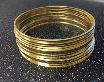 Könnte beinhalten: Ein Stapel goldfarbener Armreifen. Die Armreifen sind dünn und haben eine glatte, glänzende Oberfläche.