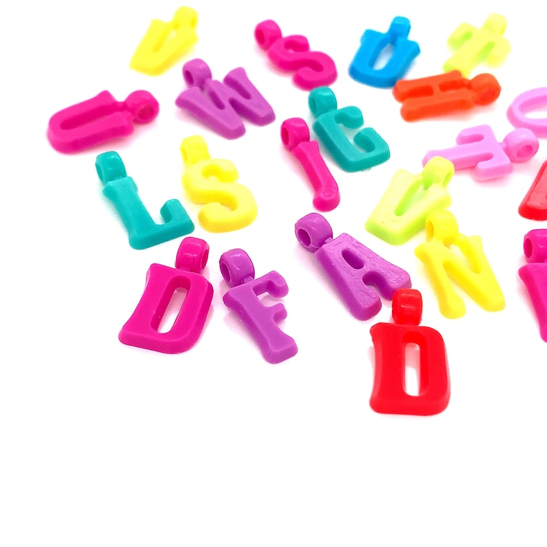 May include: Assortment of colorful plastic letter charms in various colors, including pink, purple, red, yellow, blue, green, and orange. The letters are in uppercase and are all different.