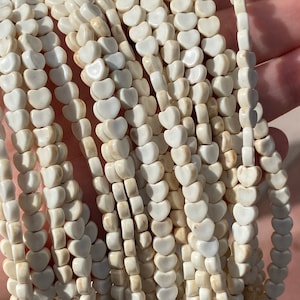 May include: A strand of white heart-shaped beads. The beads are made of a natural material with a slightly off-white color and a subtle marbled pattern.