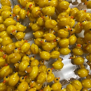 May include: A close-up of a large pile of yellow glass beads shaped like rubber duckies. The beads are strung on clear string and are arranged in a random pattern.