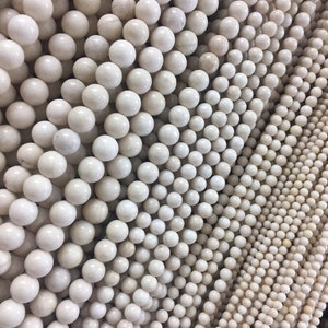May include: A close-up of a collection of white round beads, arranged in rows, creating a textured pattern.