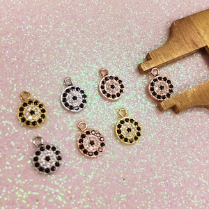 May include: Seven small, round, evil eye charms with black and white crystal accents. The charms are in different metal finishes: gold, silver, rose gold.