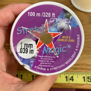 Puede incluir: Un carrete de cord&oacute;n Stretch Magic para cuentas y joyer&iacute;a. La etiqueta morada y blanca indica que el cord&oacute;n tiene 1 mm de di&aacute;metro y 100 metros de largo. La etiqueta tambi&eacute;n indica que el cord&oacute;n es fuerte, el&aacute;stico, resistente y flexible.