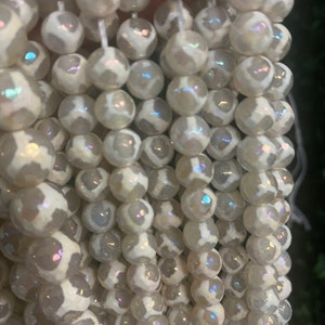 May include: A strand of white agate beads with iridescent shimmer. The beads are round and have a white and gray pattern.