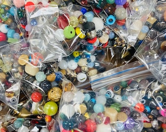 Puede incluir: Surtido de cuentas de colores en varias formas y tamaños, incluyendo cuentas redondas, cuadradas y en forma de ojo, empaquetadas en bolsas de plástico transparentes.