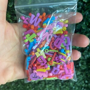 May include: A plastic bag filled with colorful letter beads in various shades of pink, purple, yellow, orange, green, and blue.