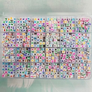 May include: A clear plastic storage box filled with small white letter beads. Each compartment contains a different letter of the alphabet, with the letters printed in various colors.