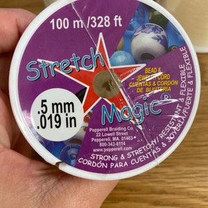Puede incluir: Un carrete de cord&oacute;n el&aacute;stico "Stretch Magic" para cuentas y joyer&iacute;a. La etiqueta es morada y blanca, con el texto "100 m / 328 ft" y ".5 mm". El cord&oacute;n es fuerte, el&aacute;stico y flexible.